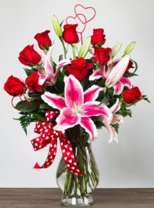 luxurious bouquet is filled with sensational red roses and fragrant stargazer lilies in a glass vase accented with a matching bow and hearts in the design