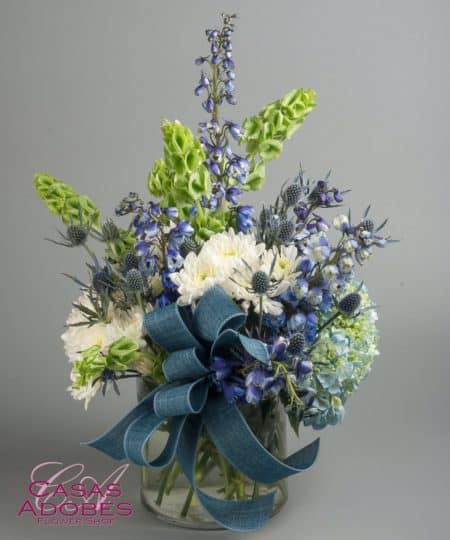 A vase holds a large spray of white and blue flowers including blue hydrangea, blue delphinium, Bells of Ireland, white chyrsanthemums and thistle. It's a beautiful design capturing the feel of the ocean in flowers. You could send this bouquet for any occasion expressing thanks, thinking of you or sympathy. 