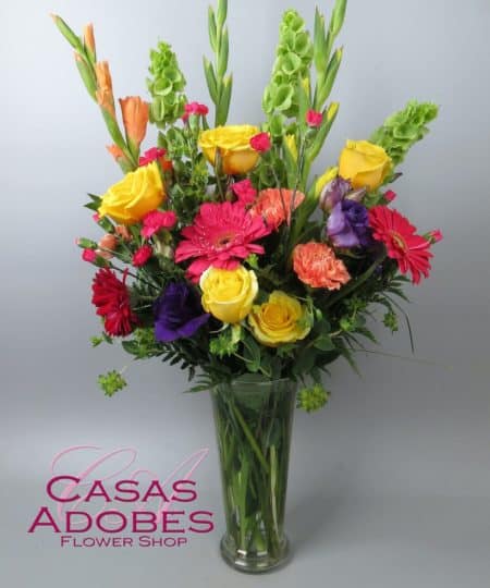 Bring the sunny side of the street indoors with this radiant array of fresh flowers in a charming vase that's as bright as a summer morning. This design features vibrant yellow gladiola, yellow roses, pink gerbera daisies, purple lisianthus, Bells of Ireland, and coral and hot pink mini carnations in a fluted glass vase. 