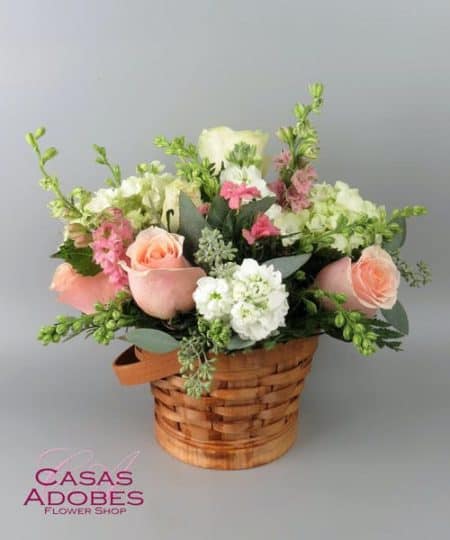 White and salmon roses made the eyes dance while surrounded by pink larkspur, clouds of white hydrangea, and lush greens, arranged to perfection in an oval stained woodchip basket that helps to blend soft sophistication with raw, rustic appeal.