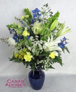 This bouquet pairs pure white flowers with deep blue blooms and accents of sunny yellow in a gorgeous blue glass vase. Blooms such as Bells of Ireland, blue iris, blue delphinium, white roses, white snapdragons, graceful white lilies, yellow alstroemeria,, yellow mini carnations and delicate Queen Anne's lace are accented by eucalyptus and fern in a stunning cobalt blue glass vase.