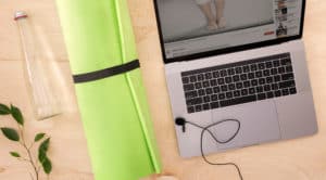 Green yoga mat on wooden floor with open laptop and water bottle
